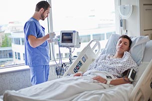 un homme debout &agrave; c&ocirc;t&eacute; d'un patient dans un lit d'h&ocirc;pital