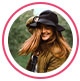 Image de profil d&rsquo;une consommatrice, une femme rousse sourit et porte un chapeau noir.