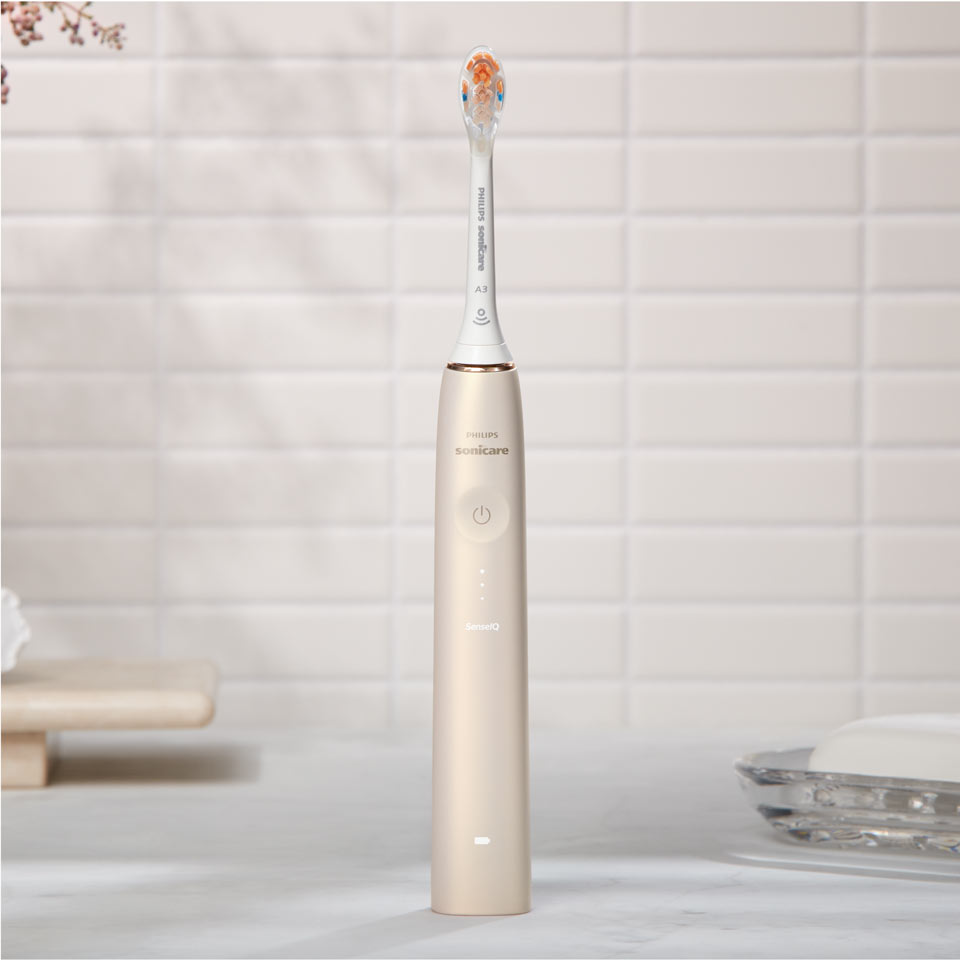 Brosse &agrave; dents &eacute;lectrique Philips&nbsp;Sonicare Prestige&nbsp;9900 avec la t&ecirc;te de brosse tout-en-un pos&eacute;es sur un plan de travail