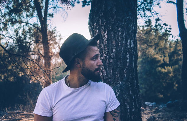 Un homme de profil avec un chapeau et une barbe de hipster se trouve dans la for&ecirc;t.