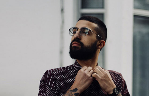 Un homme avec une barbe compl&egrave;te boutonne le haut de sa chemise.