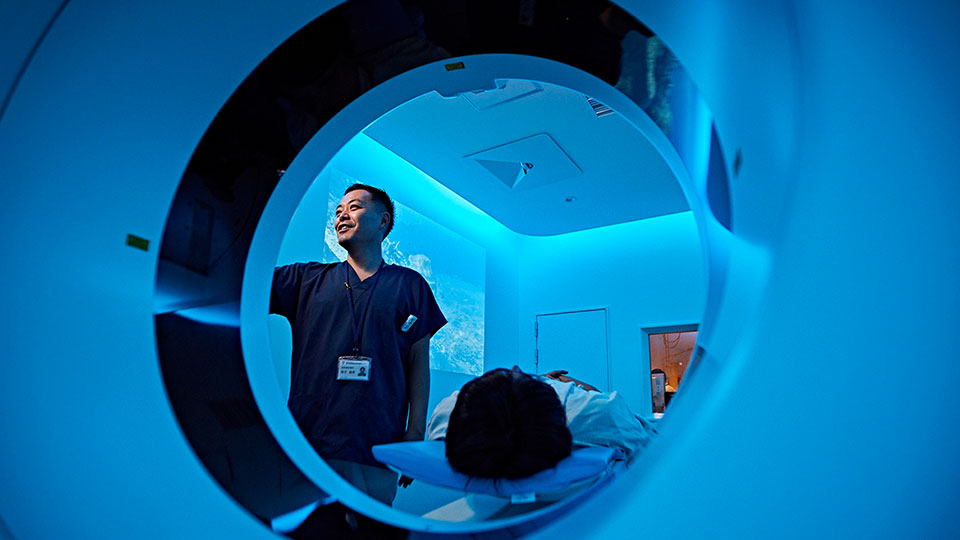 Photo d&rsquo;un manipulateur qui configure une acquisition sur le statif du scanner, avec le patient sur la table d&rsquo;examen