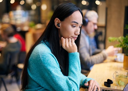 Femme &eacute;tudiant dans un caf&eacute; utilisant un casque sans fil &agrave; r&eacute;duction de bruit Philips T3508