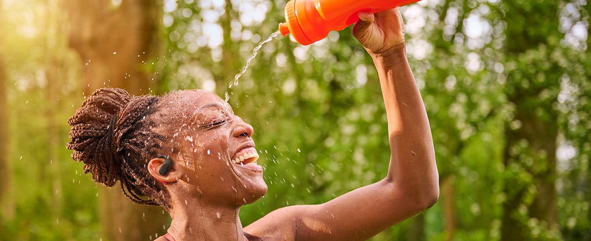 Femme se rafra&icirc;chissant en versant de l&rsquo;eau sur sa t&ecirc;te tout en portant des &eacute;couteurs de sport Philips en ext&eacute;rieur
